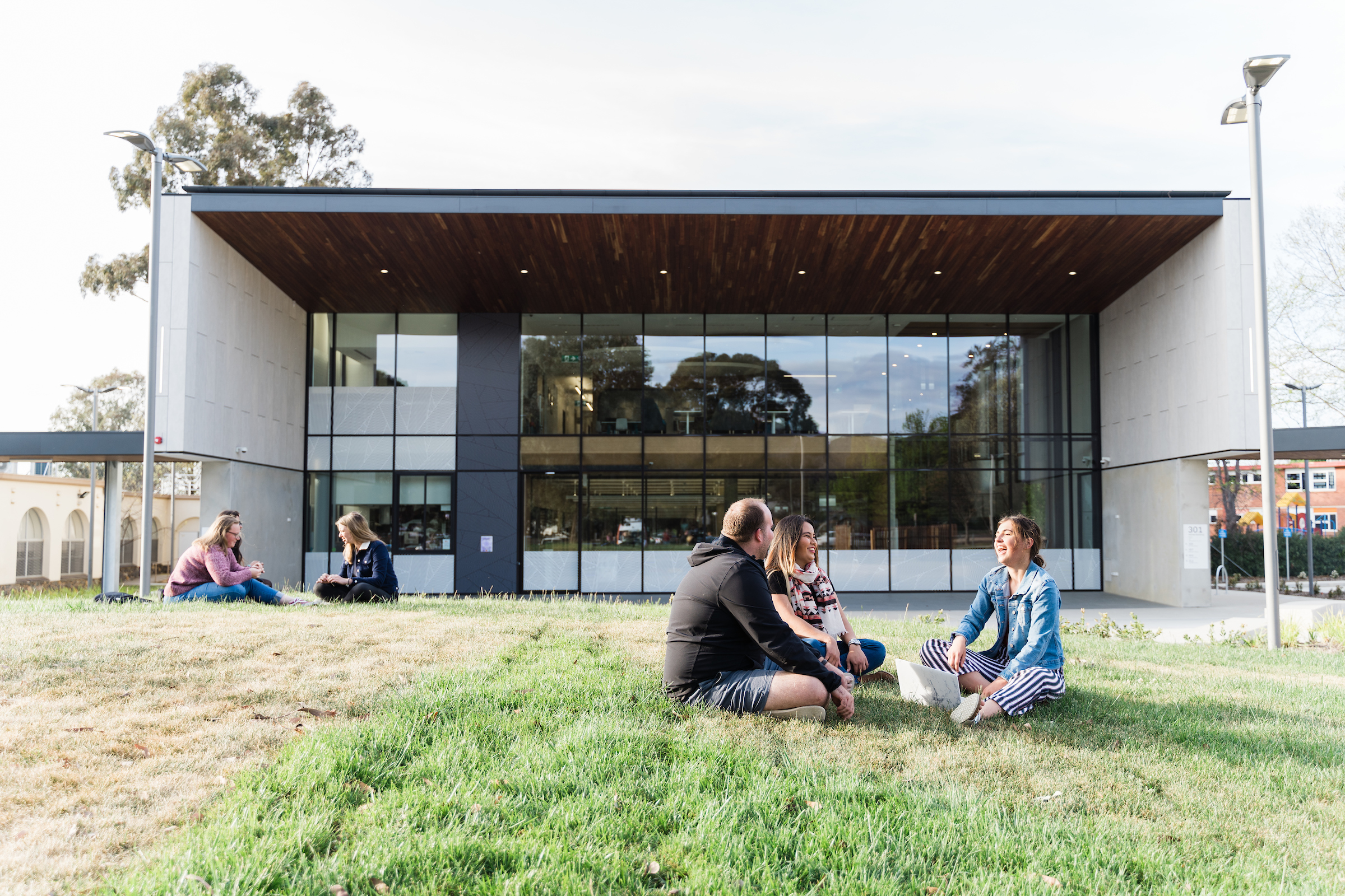  students sitting on green lawn infront of ACU Canberra library